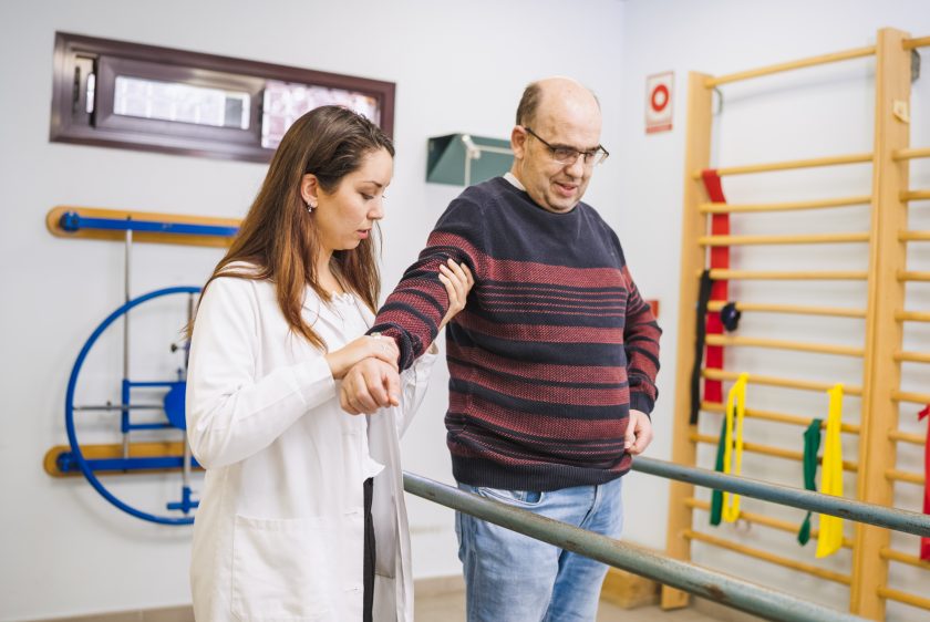 Physiotherapist assisting patient walking with disability during rehabilitation